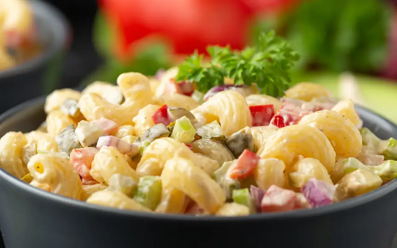 Cremiger Nudelsalat mit Schinken, Gurken, Paprika und Zwiebeln, garniert mit Petersilie. Ein Klassiker f&uuml;r jede Gelegenheit.