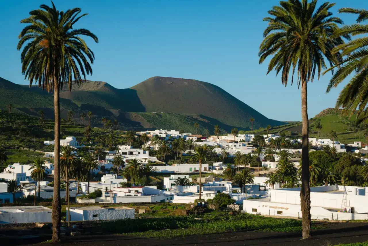 Das Tal der tausend Palmen auf Lanzarote, mit wei&szlig;en H&auml;usern und gr&uuml;nen H&uuml;geln im Hintergrund.