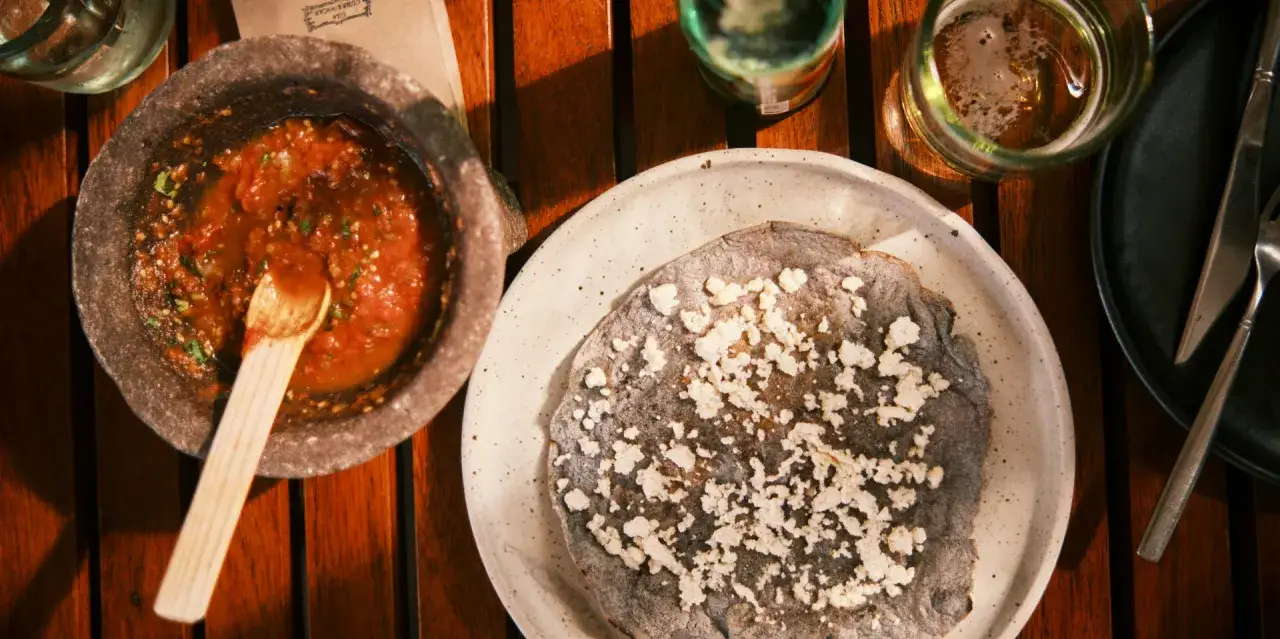Un tlayoyo de ma&iacute;z azul con queso fresco y salsa roja en molcajete. Una probadita de lo que puedes ver en M&eacute;xico.