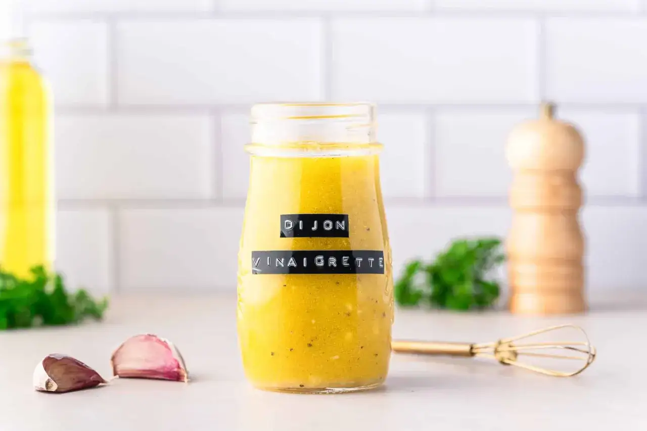 Bocal de vinaigrette maison Dijon, avec des gousses d'ail et un petit fouet à proximité.