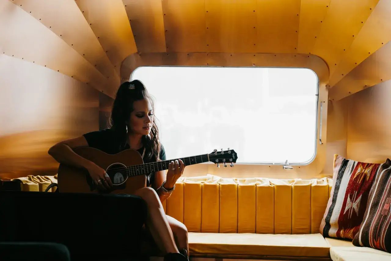 Sarah Jones, piosenkarka, gra na gitarze w przytulnym wnętrzu.