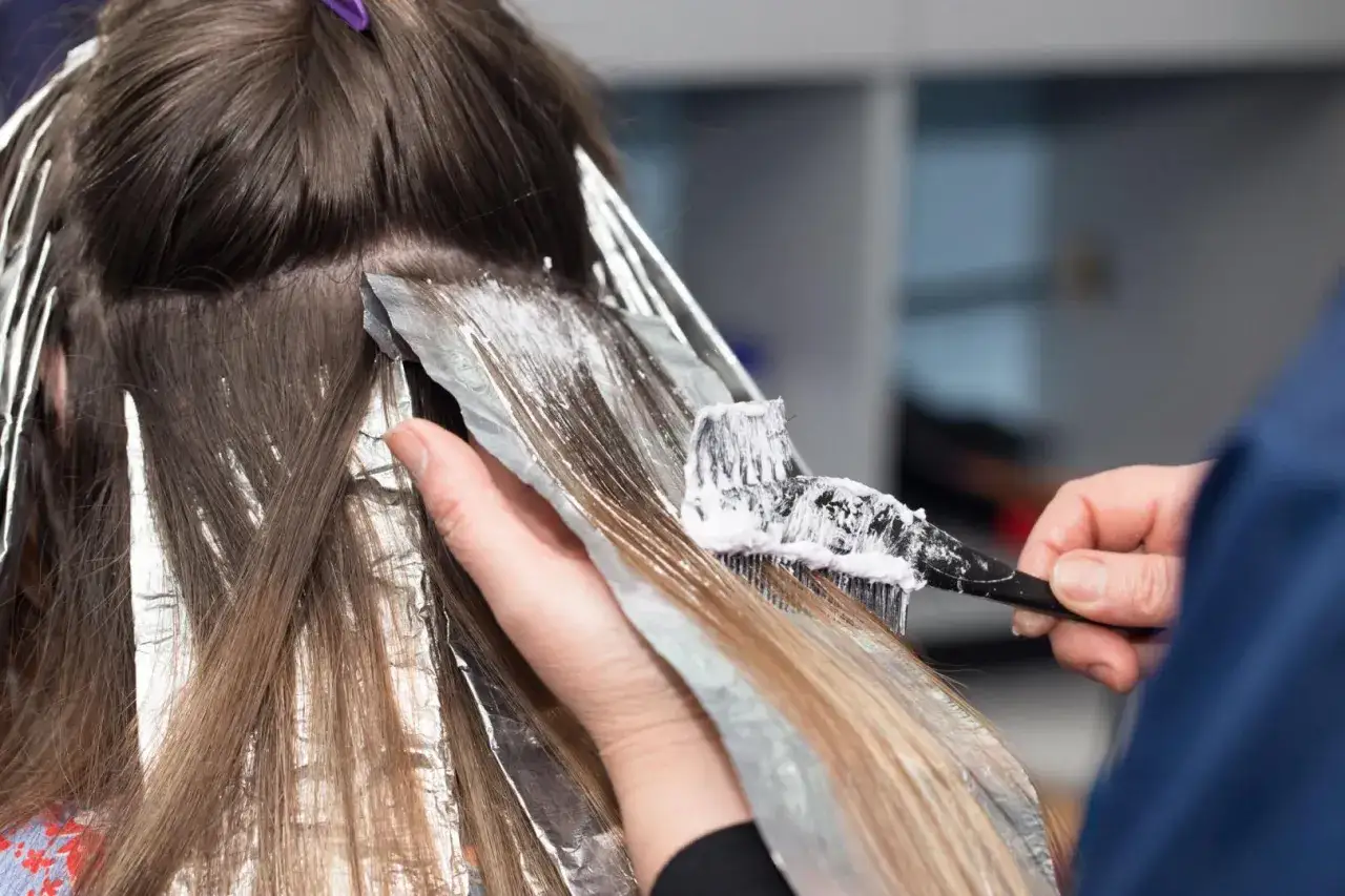 Coiffure en cours : application de produit décolorant sur des mèches. Pour savoir combien coûte une permanente, il faut consulter un professionnel.