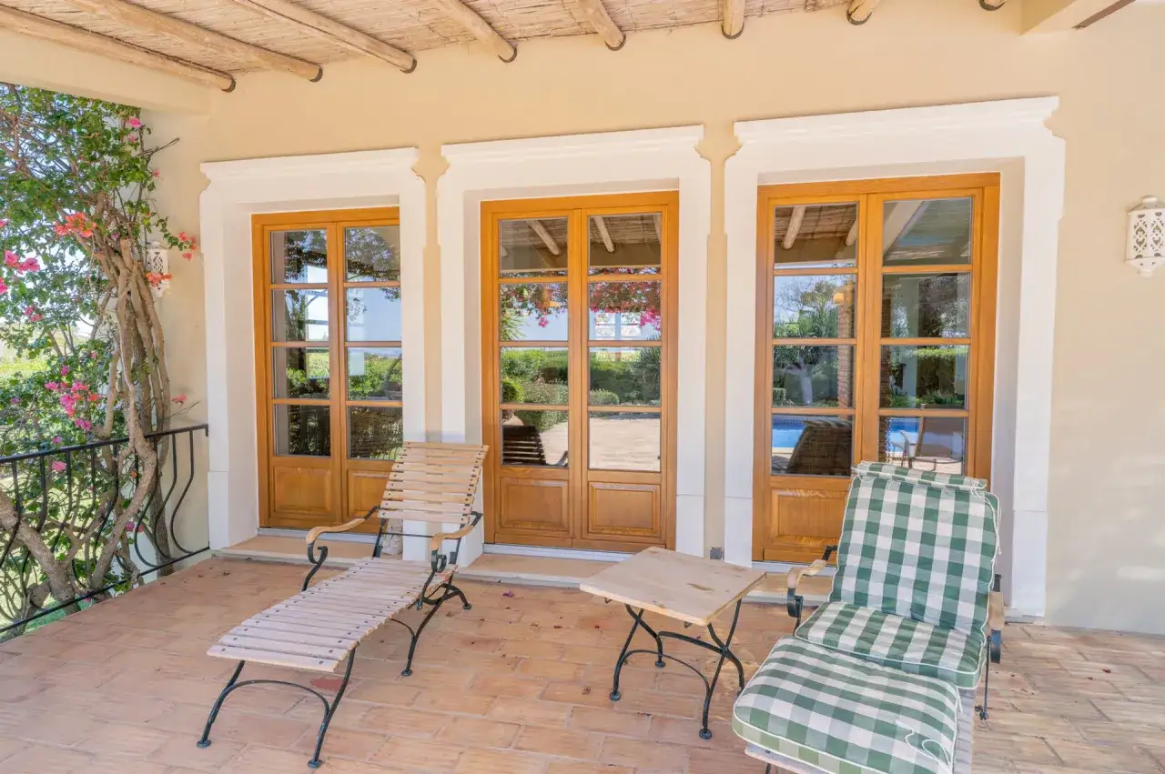 Terraza con tumbonas y mesa, puertas de madera de accoya que dan a un jardín con piscina.