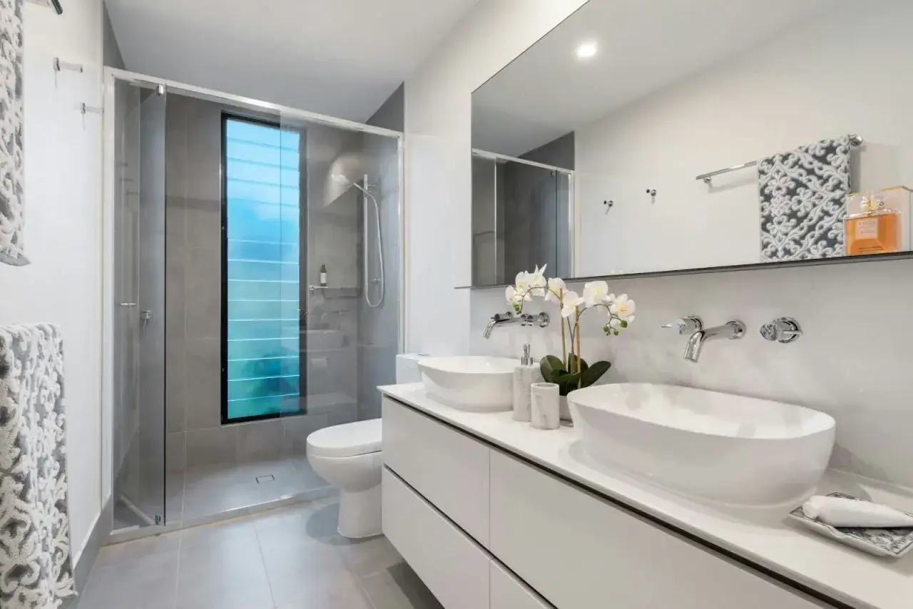 Elegantes ba&ntilde;os peque&ntilde;os con ducha, lavabos sobre encimera y ventana con persianas azules.