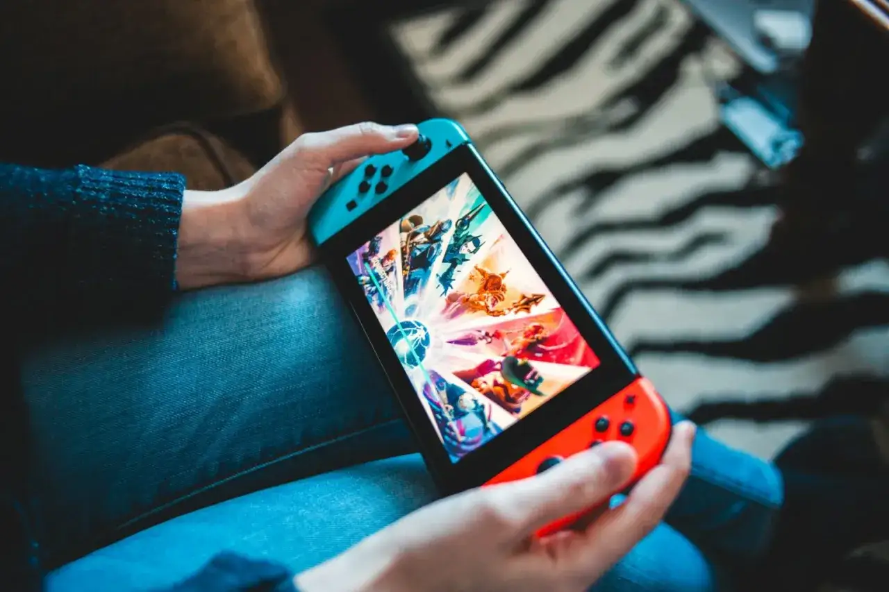 Osoba gra na konsoli Nintendo Switch w grę z kolorowymi postaciami. Konsola jest w języku polskim.