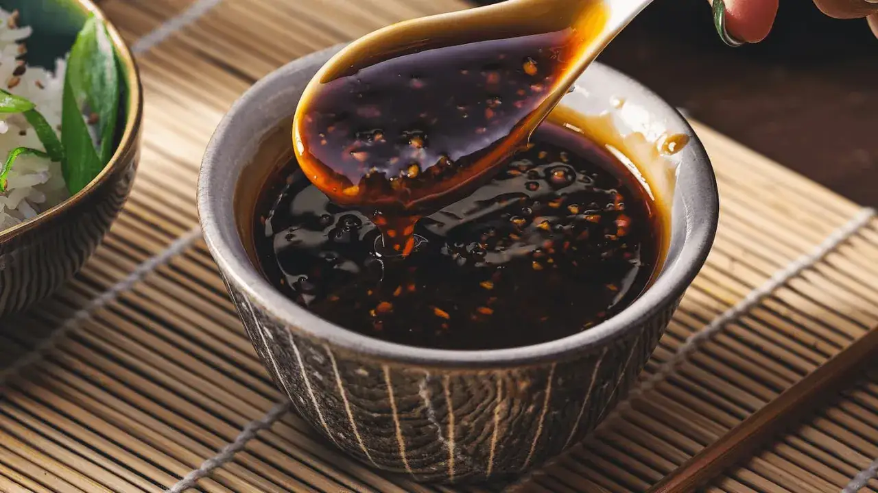 Ein Löffel hebt glänzende, dunkle Teriyaki-Sauce aus einer Schale. Perfekt für Ihr Teriyaki-Sauce-Rezept!