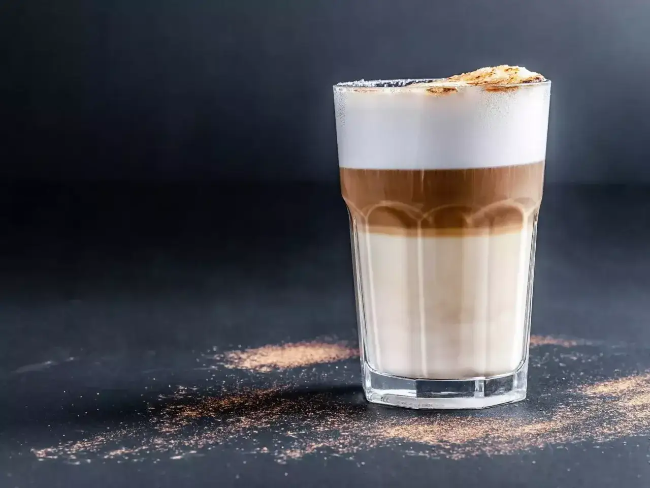 Ein geschichteter Latte Macchiato im Glas, mit cremigem Milchschaum und Kakaopulver bestreut.