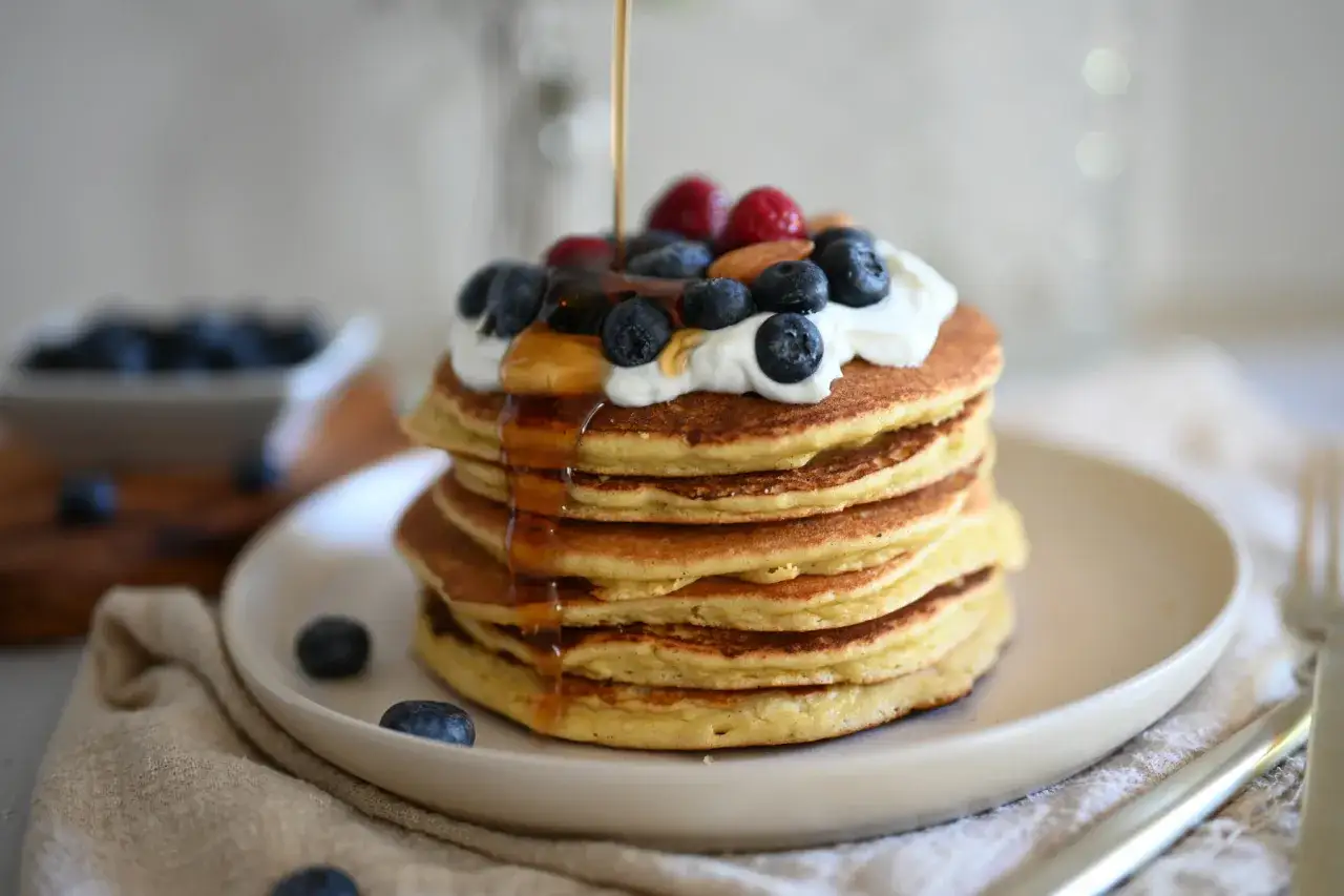 Pancake con yogurt, mirtilli e sciroppo d'acero che cola. Una deliziosa colazione.