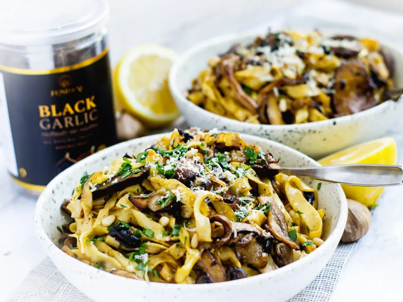 Pasta mit Pilzen und schwarzem Knoblauch, garniert mit Petersilie und Pinienkernen. Ein Glas 