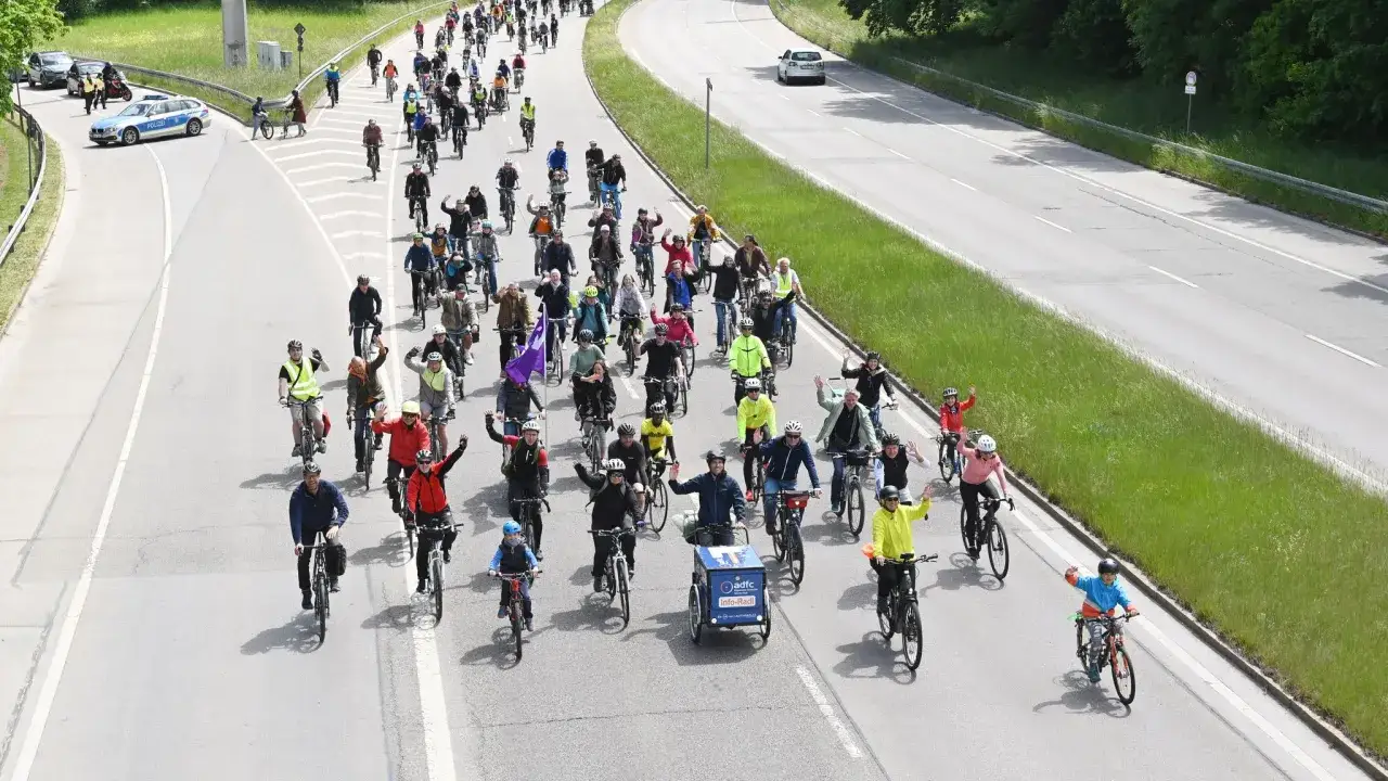 Große Fahrrad-Community fährt gemeinsam auf der Straße. Viele Menschen auf Fahrrädern, einige winken.
