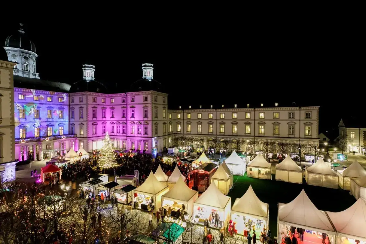 Einzigartiger Weihnachtsmarkt Bensberg vor beleuchtetem Schloss. Stände und ein Weihnachtsbaum schaffen festliche Atmosphäre.