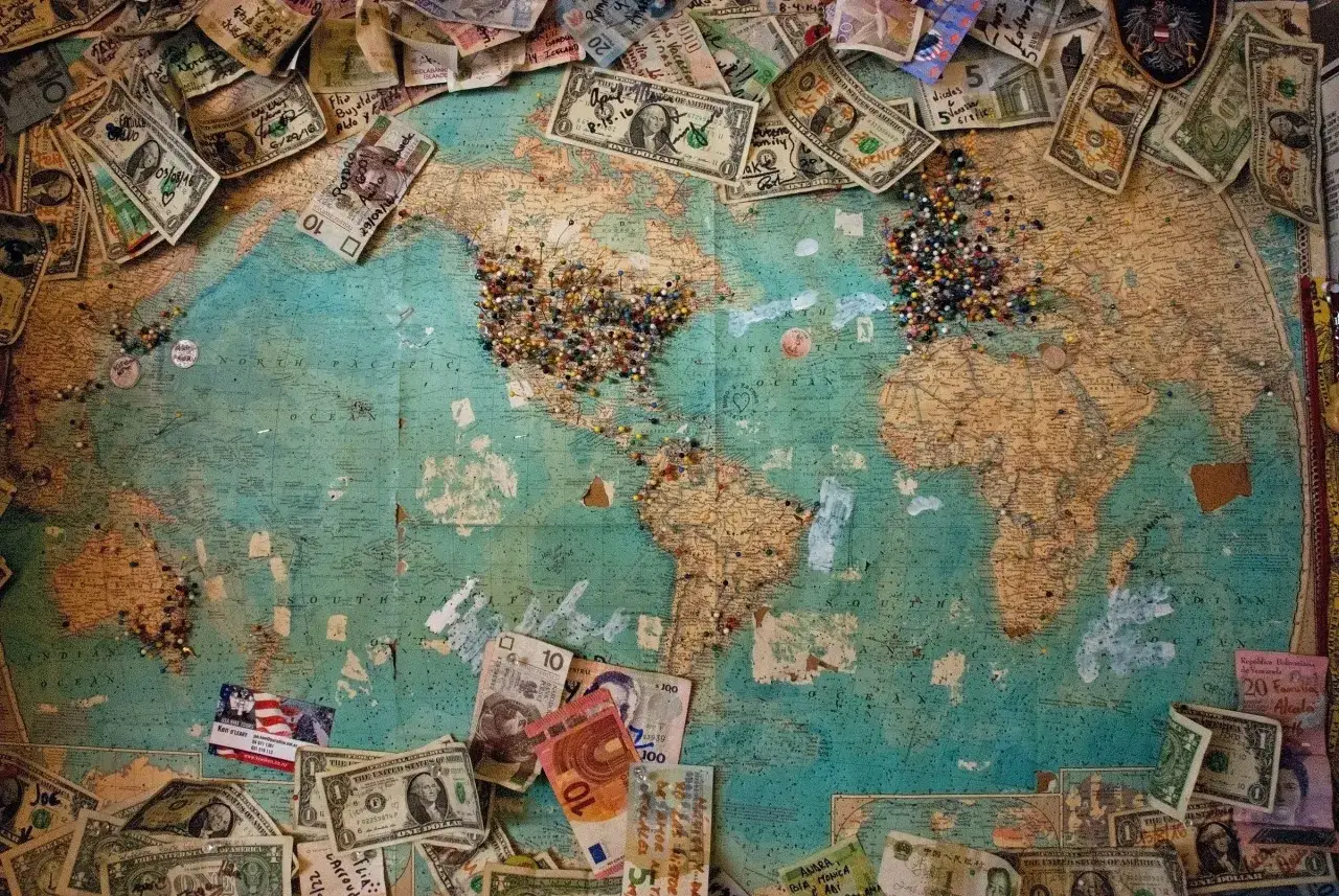 Mapa świata z pinezkami i banknotami, symbolizująca podróżowanie po świecie i marzenia o dalekich wyprawach.