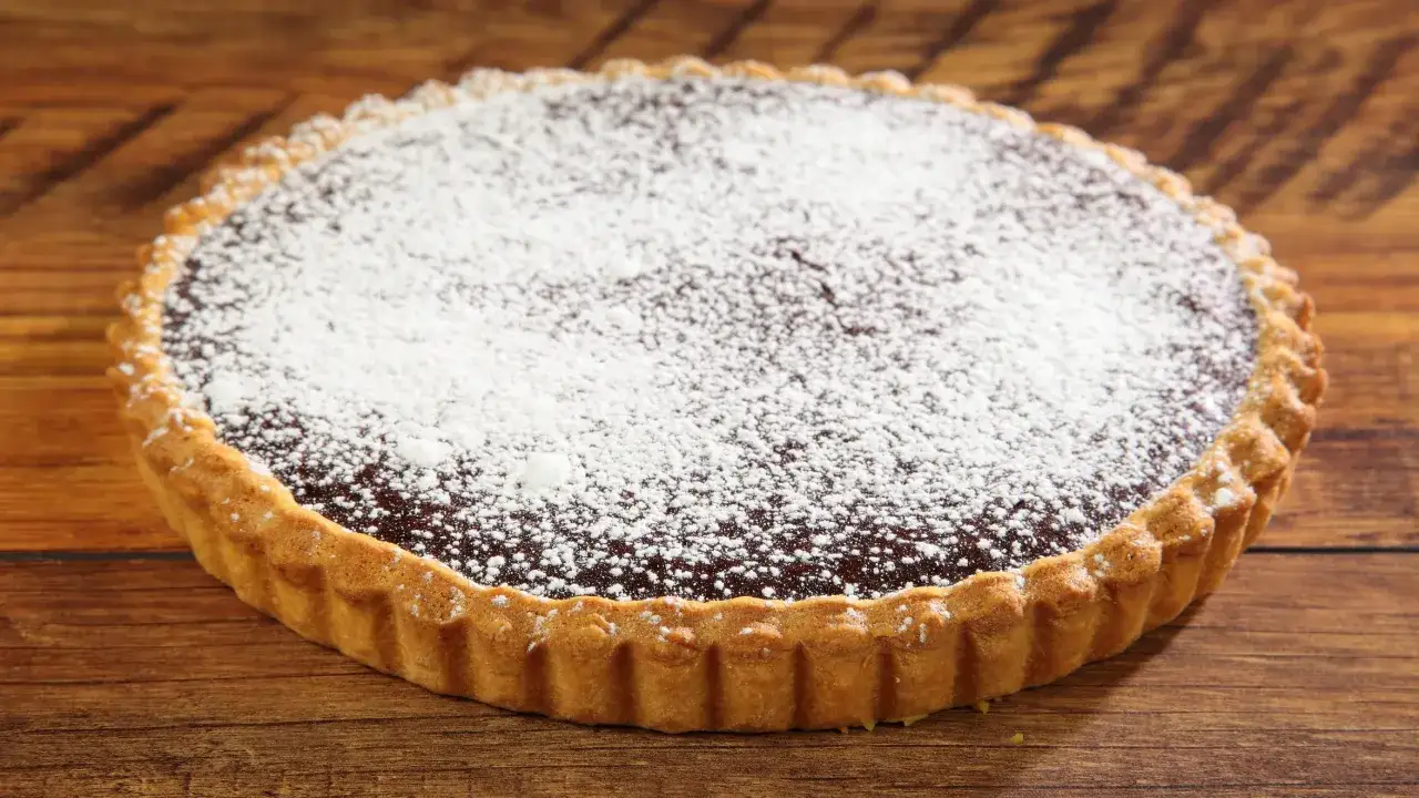 Una deliziosa crostata al cioccolato, con bordo dorato e ripieno scuro cosparso di zucchero a velo, su un tavolo di legno.