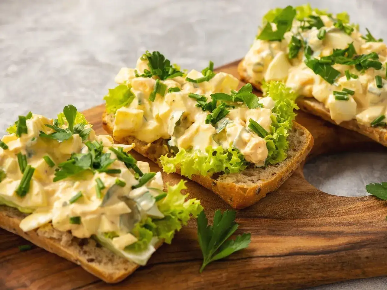 Pyszna pasta jajeczna z twarogiem na chlebie, udekorowana sałatą i szczypiorkiem. Idealna na śniadanie.