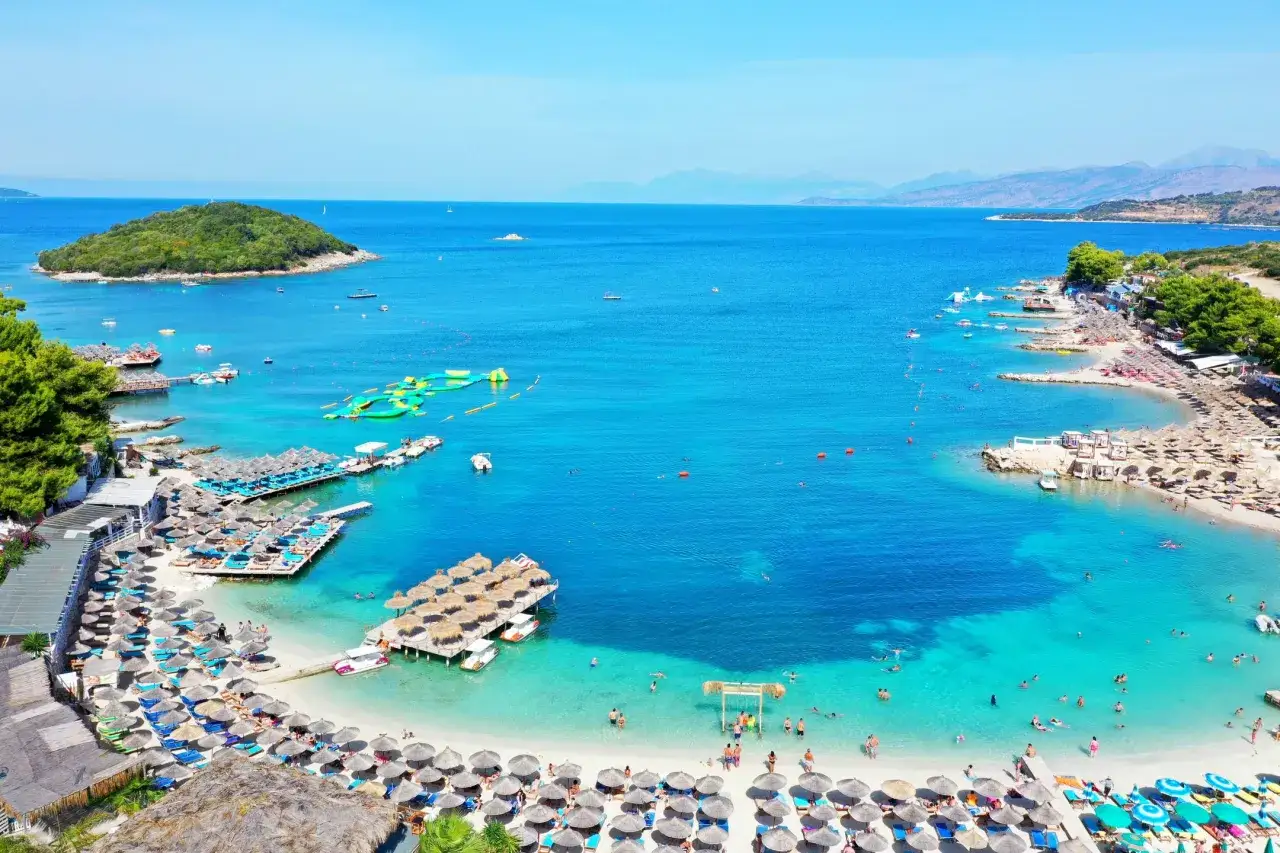 Malownicze **albania plaże** z turkusową wodą, wyspą, leżakami i parasolami.