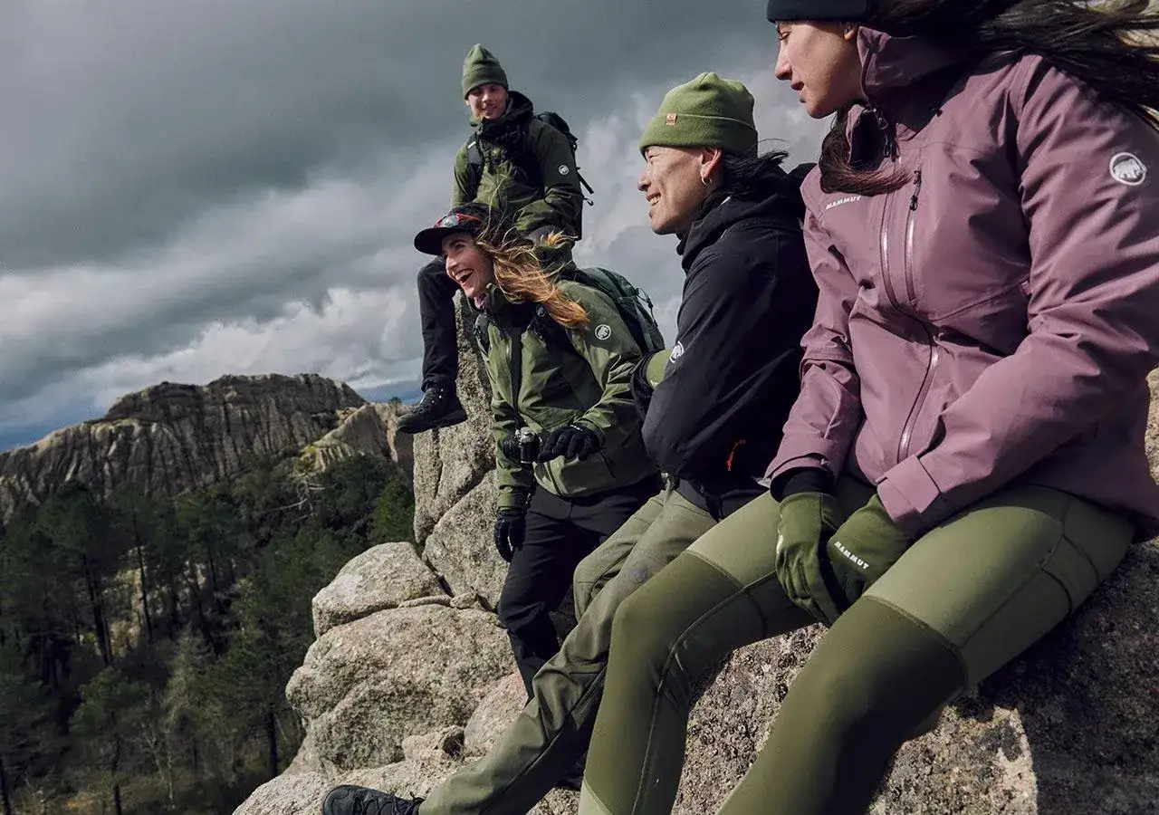 Grupa przyjaci&oacute;ł w zielonych czapkach i kurtkach, podziwiająca widok. Jaki softshell sprawdzi się w g&oacute;rach? Ten wygląda idealnie!