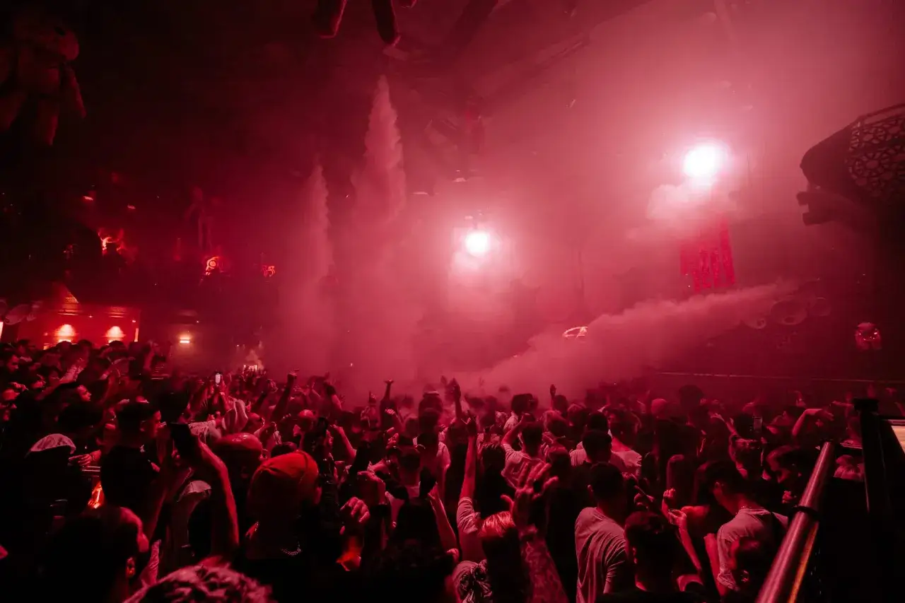 Folla in delirio in un club di Londra, tra fumo rosso e luci stroboscopiche.