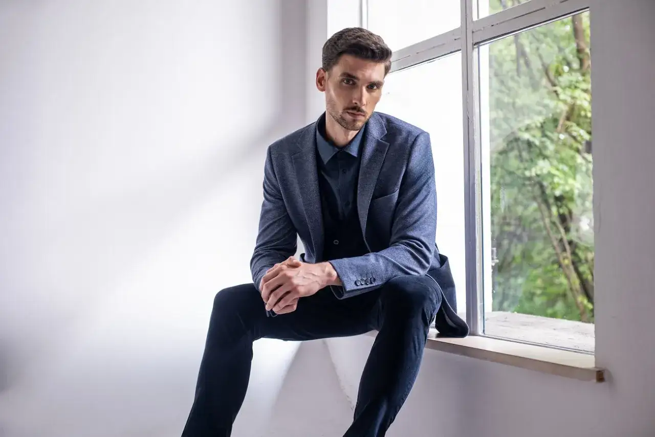 Elegancki mężczyzna w granatowej koszuli i marynarce, zastanawia się, jaki krawat do niebieskiej koszuli będzie najlepszy.