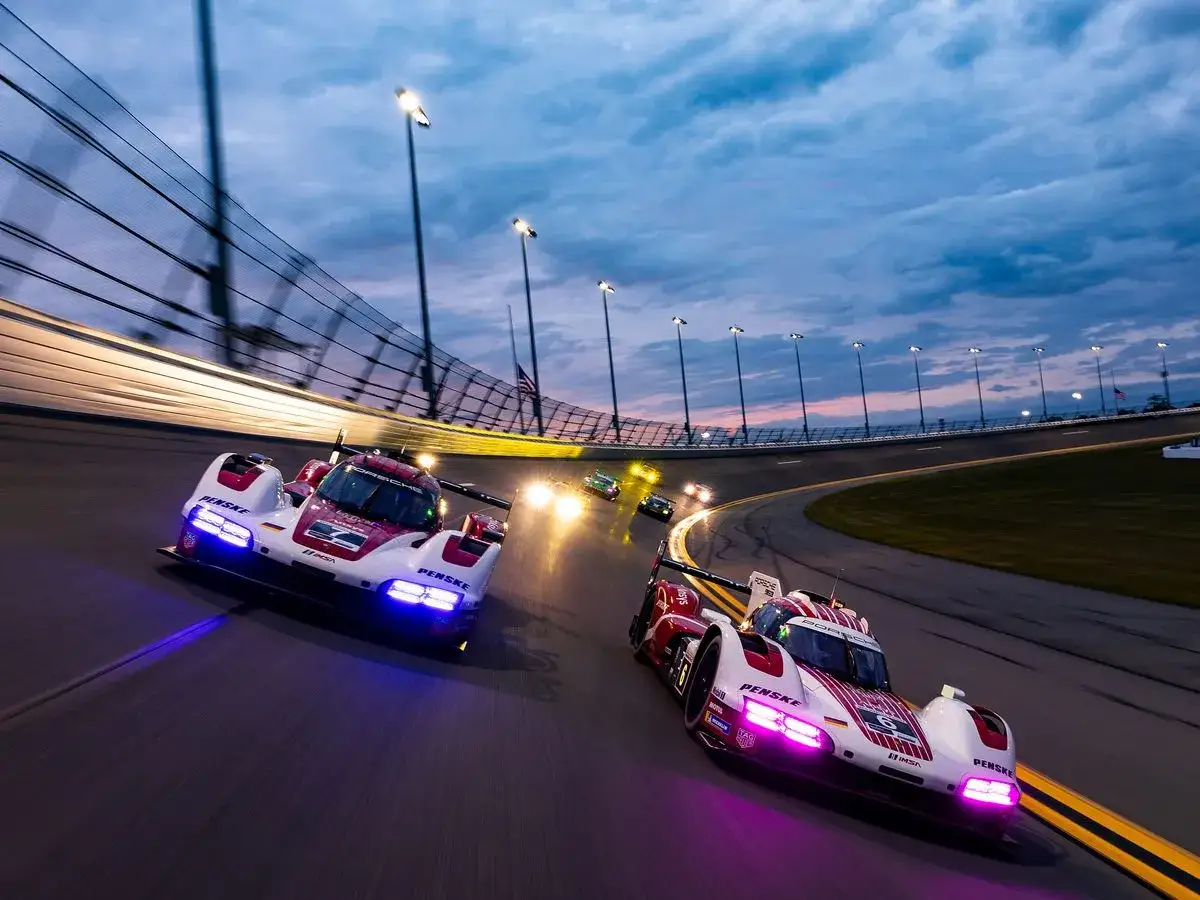 Zwei Rennwagen rasen im D&auml;mmerlicht &uuml;ber die Strecke. Das 24-Stunden-Rennen von Daytona ist in vollem Gange, die Scheinwerfer der Autos leuchten hell.