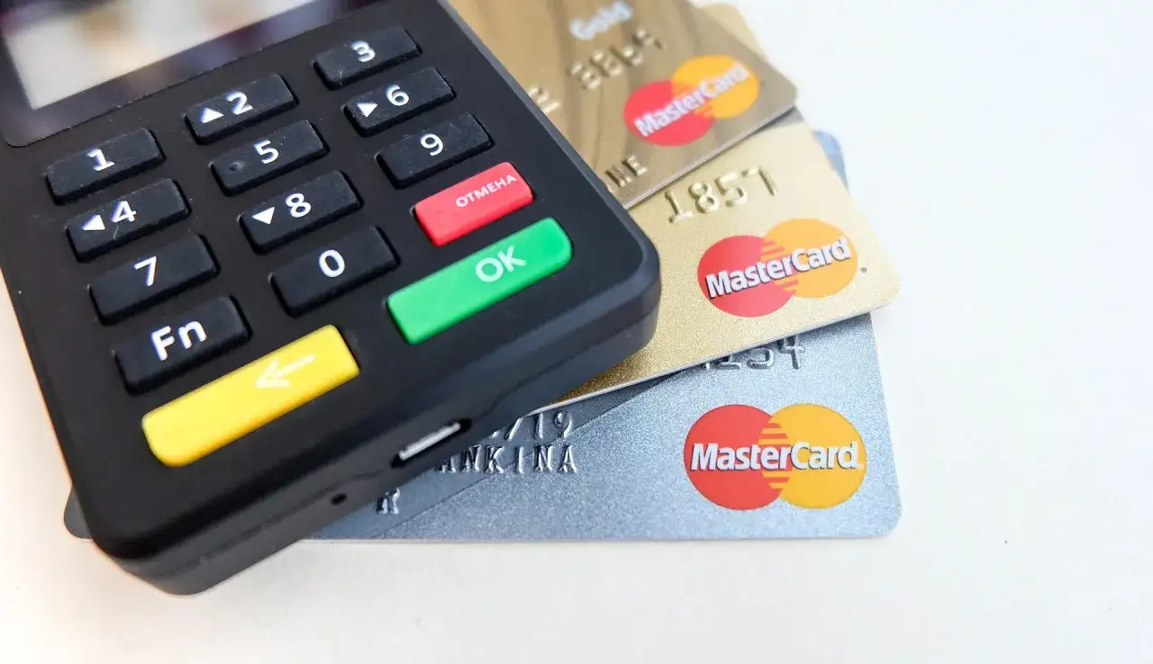 Terminal płatniczy z klawiaturą i przyciskami OK/OTMEHA obok stosu kart MasterCard. Szybkie płatności z bancontact.
