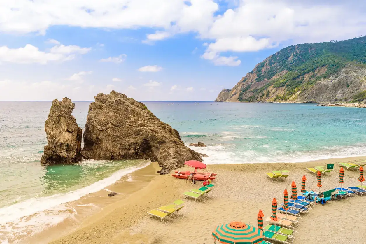 Spiagge di sabbia in Liguria con scogli imponenti, mare azzurro e lettini pronti per il relax.