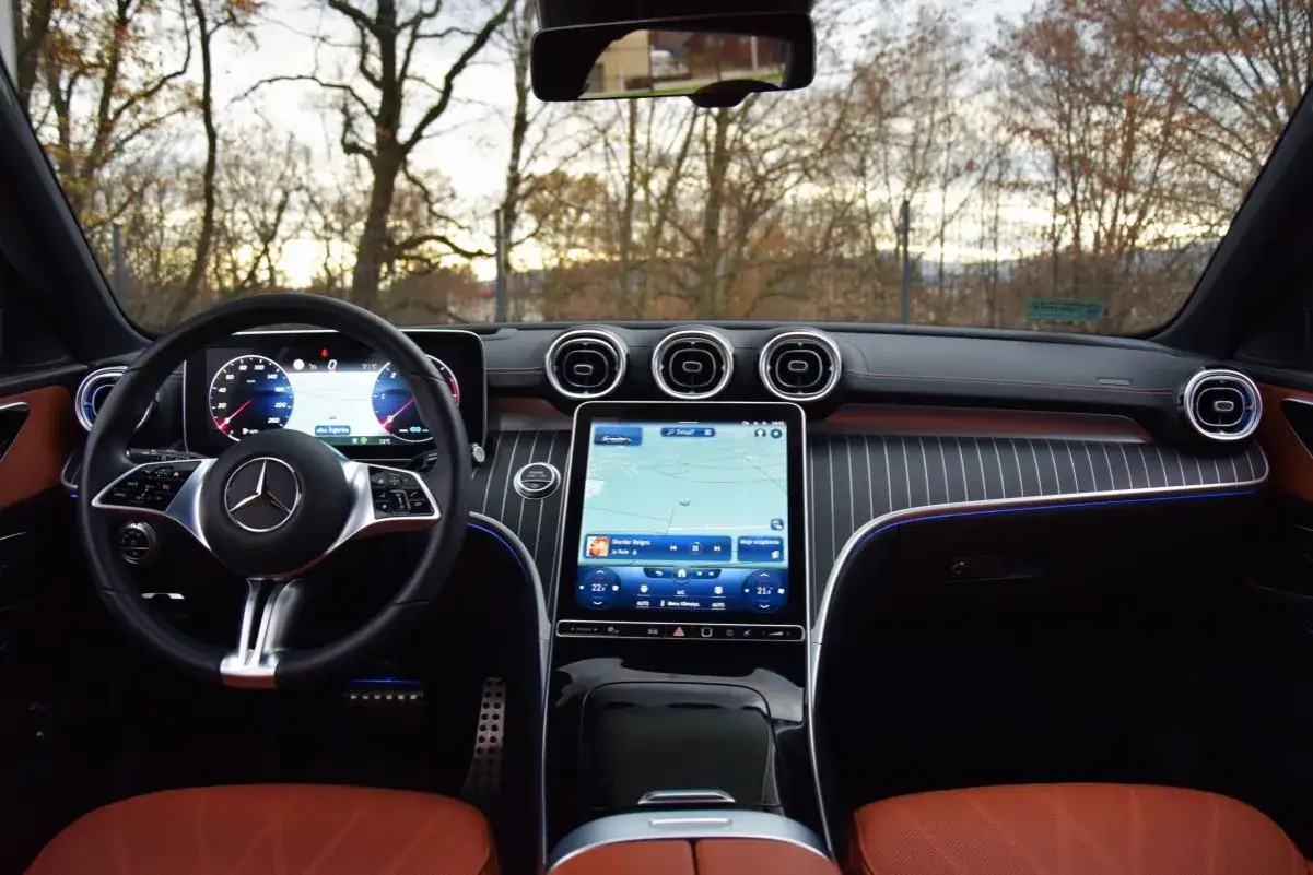 Wnętrze Mercedesa C 220 d z cyfrowymi zegarami, dużym ekranem multimedialnym z nawigacją i brązową skórzaną tapicerką.