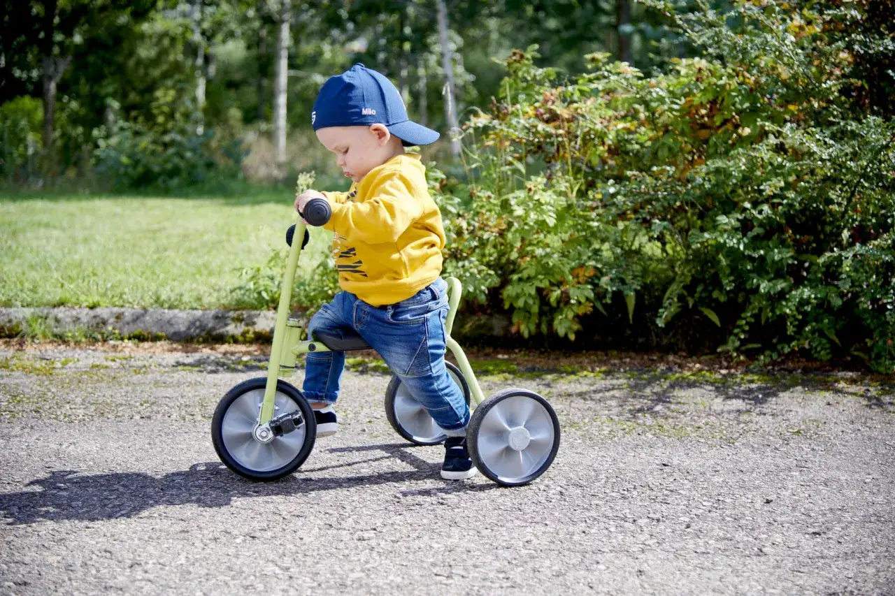 Liten pojke i gul tr&ouml;ja och keps p&aring; en gr&ouml;n trehjuling. En h&auml;rlig bild som f&aring;ngar gl&auml;djen i att uppt&auml;cka v&auml;rlden i r&auml;tt trehjuling &aring;lder.