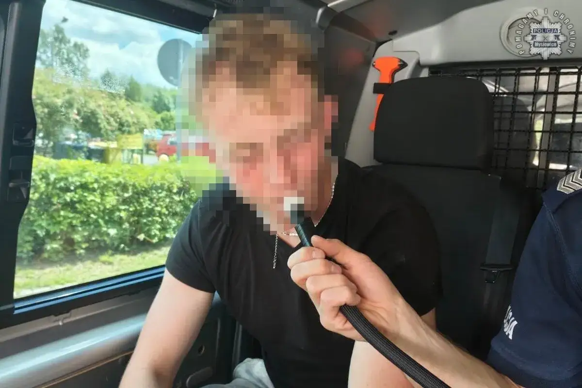 Mężczyzna dmucha w alkomat w radiowozie. Policja prowadzi czynności w sprawie konfiskaty samochodu.