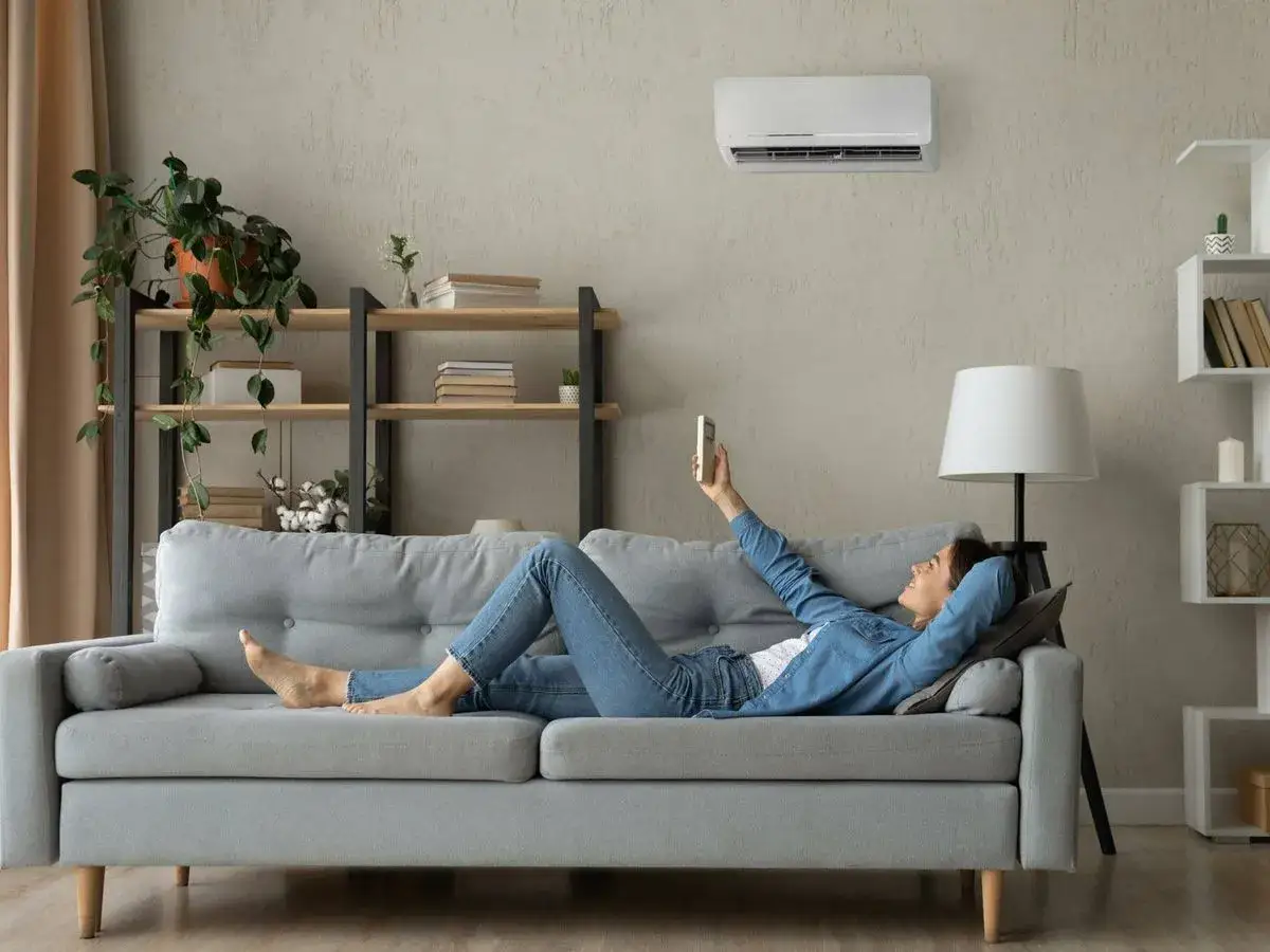 Mujer relajada en sofá, disfrutando de la temperatura ideal aire acondicionado.