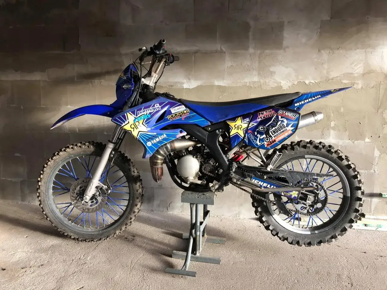 Niebieski motocykl Yamaha DT 50 z naklejkami Rockstar i Michelin, gotowy do jazdy. Dane techniczne tego modelu są imponujące.