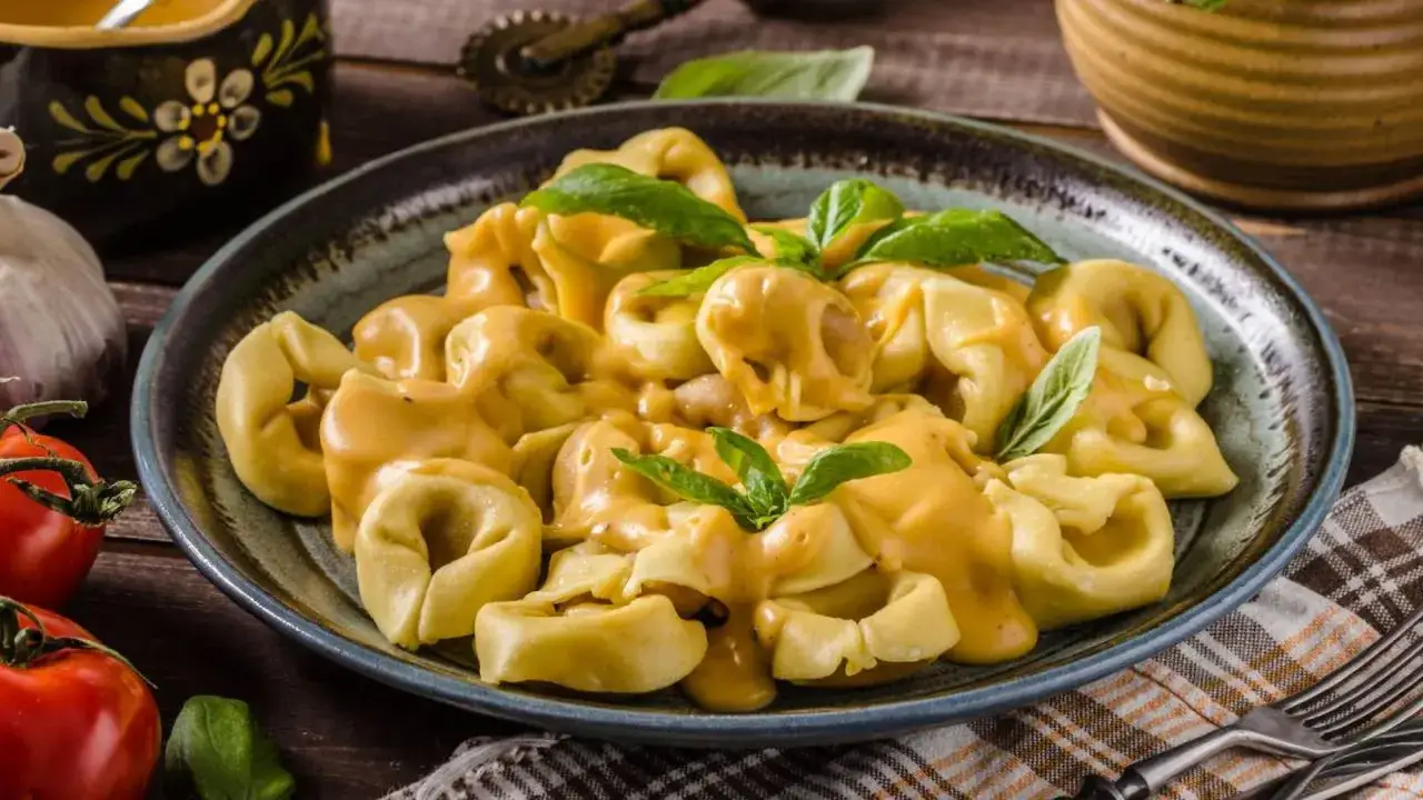 Un plato de tortellini de queso cubiertos con una cremosa salsa, decorados con hojas de albahaca fresca.