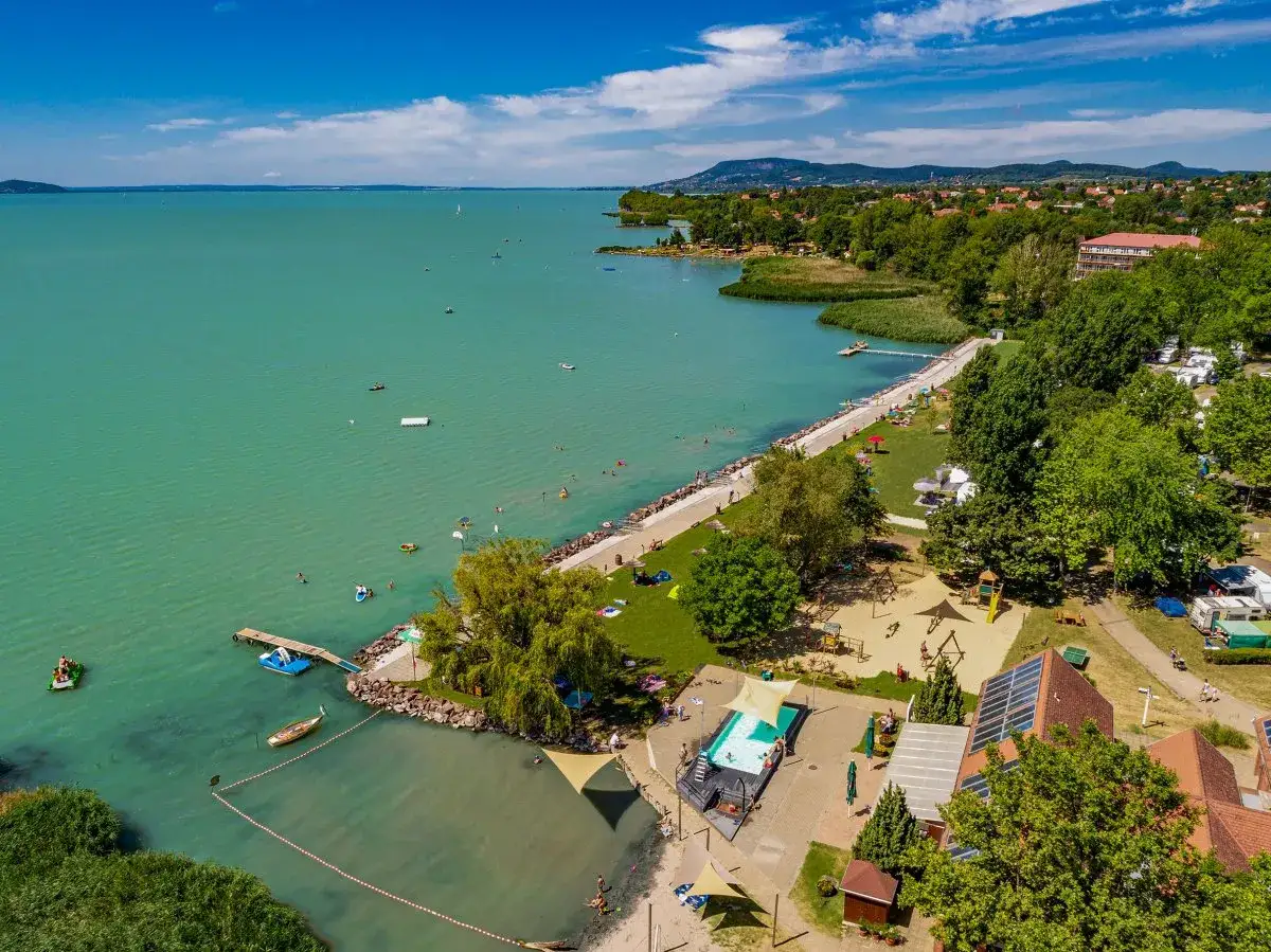 Słoneczny dzień na kempingu Balaton. Ludzie kąpią się w jeziorze i basenie, pływają łódkami.