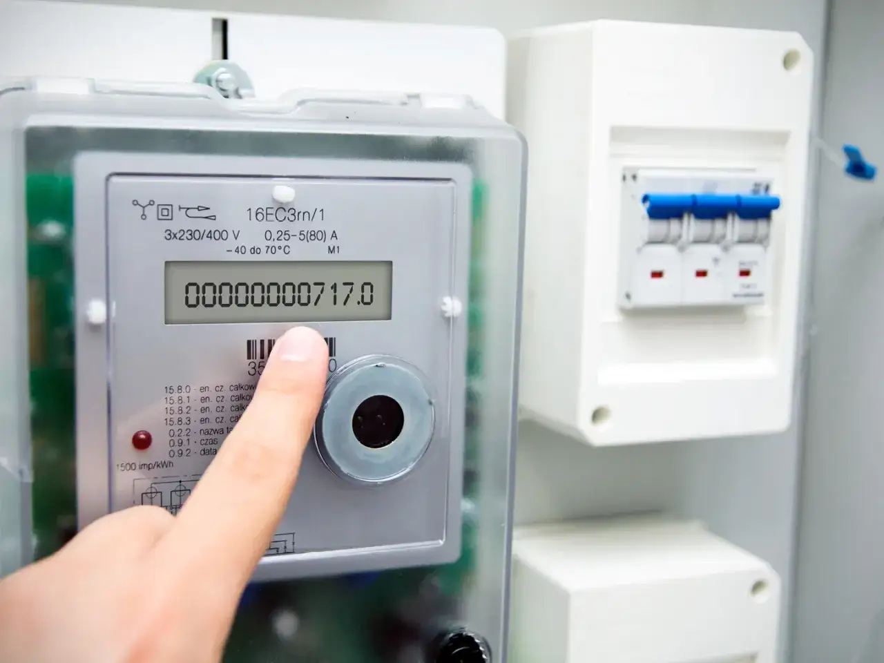 Palec wskazuje licznik energii elektrycznej. To urządzenie pomoże oszacować roczne zużycie gazu w domu 100m2.