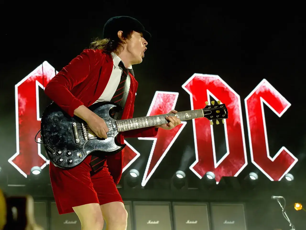 Angus Young z AC/DC gra na gitarze w czerwonym stroju, wykonując AC DC największe przeboje.