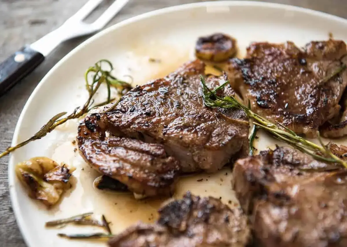 Saftiges Lamm anbraten, mit Rosmarin und Knoblauch garniert, auf einem Teller serviert.