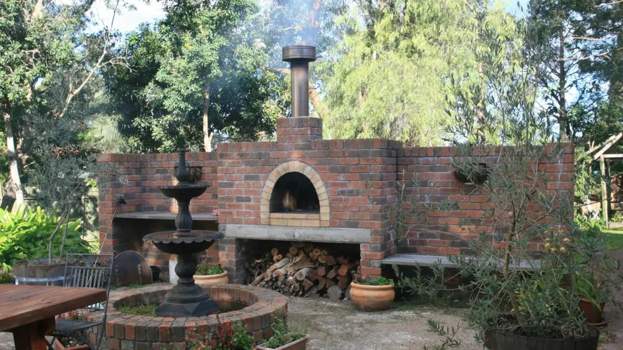 En vacker tegelbyggd pizzaugn med en fontän och sittplatser i trädgården. Perfekt för att bygga pizzaugn och njuta av utomhuslivet.