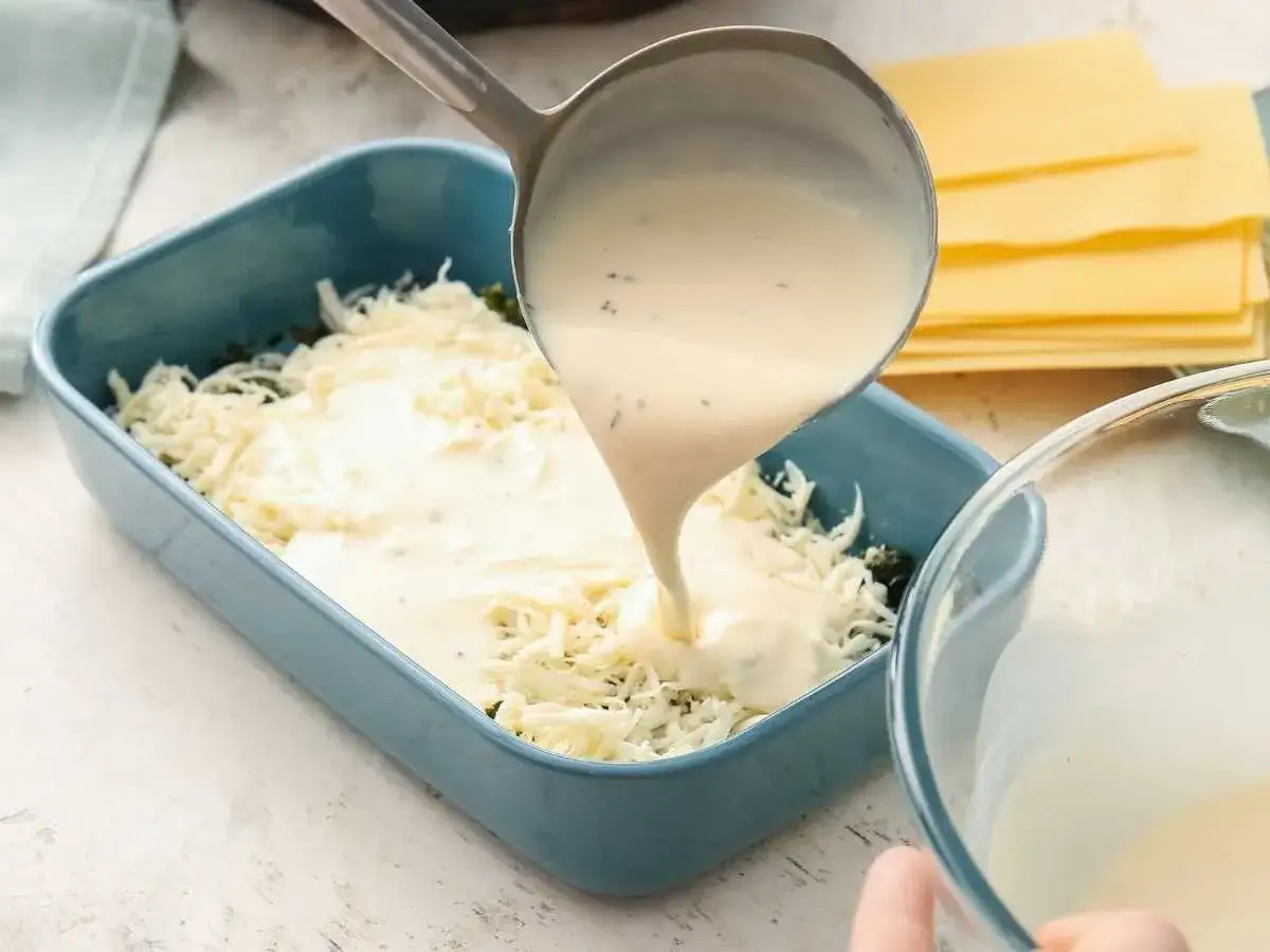 Se vierte bechamel para lasaña sobre queso rallado en un plato azul.