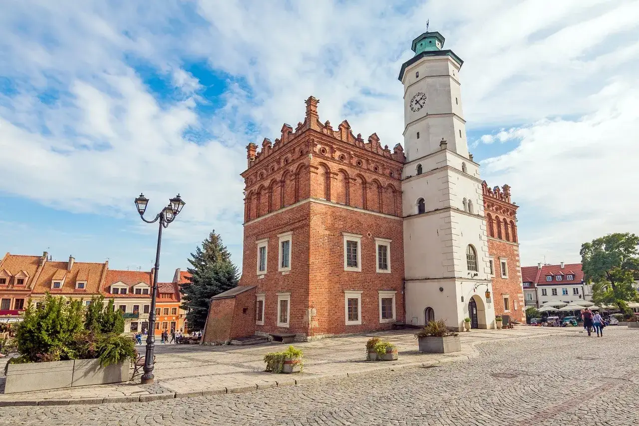 Ratusz w Sandomierzu nad Wisłą, z ceglaną wieżą i zegarem, na brukowanym rynku.