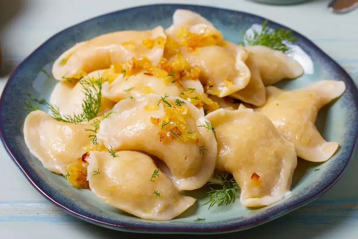 Pyszne pierogi z delikatnym farszem, posypane skwarkami i koperkiem, na talerzu.