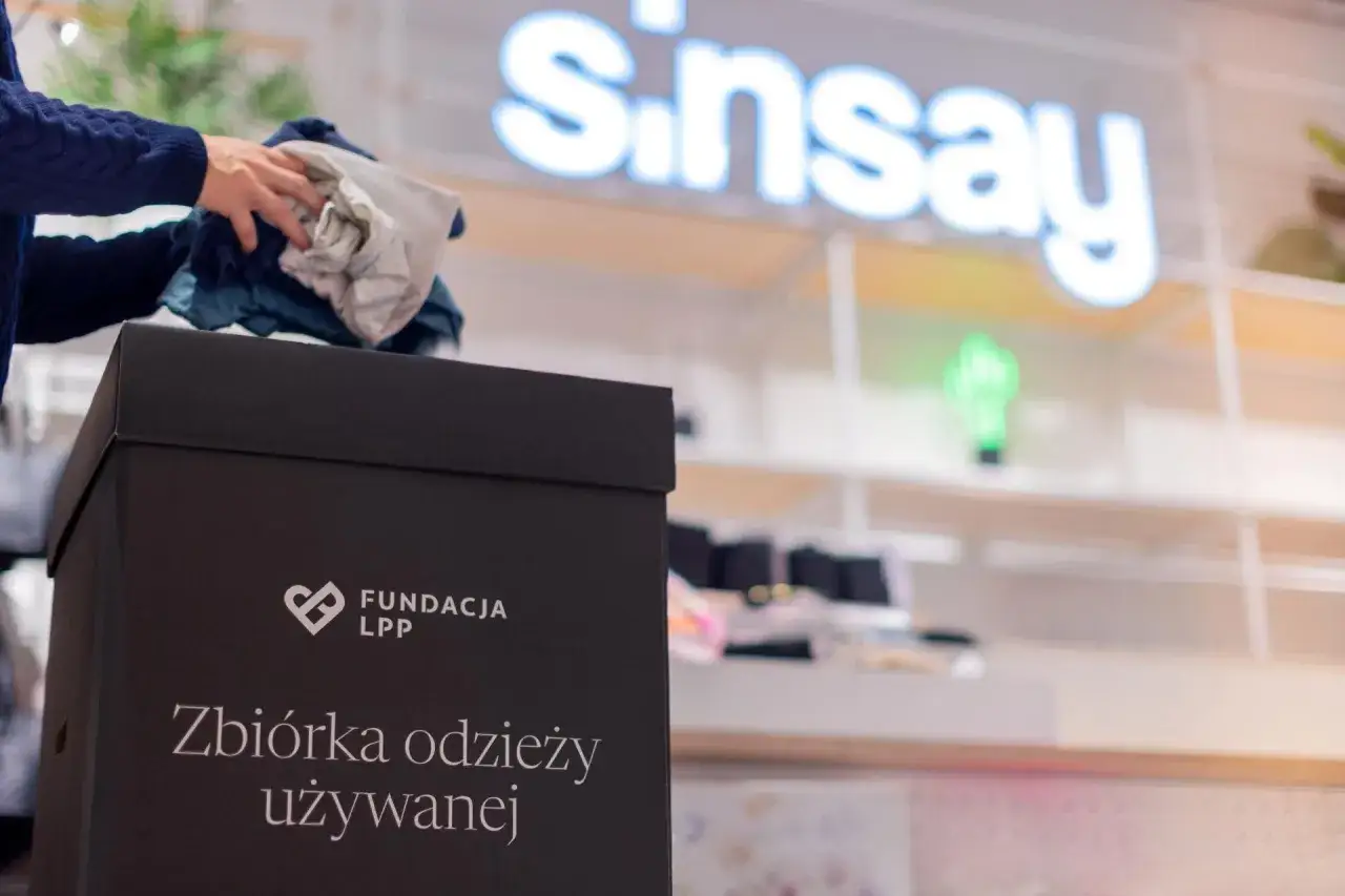 Ręce wkładają ubrania do czarnego pudła z napisem