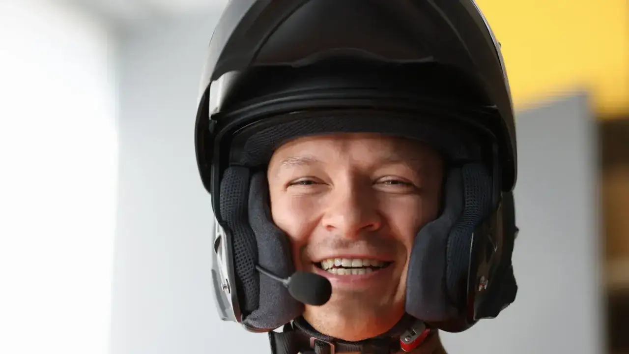 Hombre sonriente con casco de moto y micr&oacute;fono, listo para usar su intercomunicador moto legal y comunicarse en ruta.
