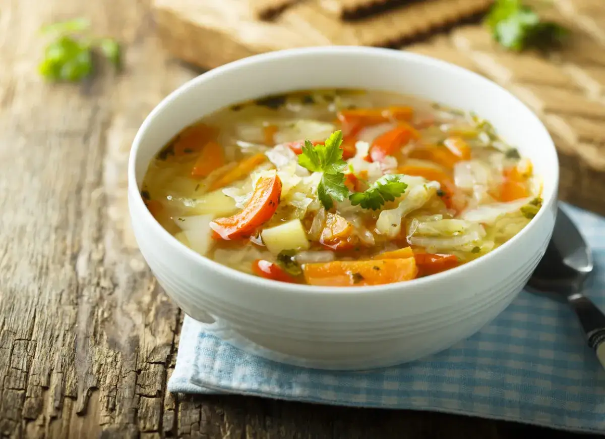 Aromaticzna, tradycyjna zupa jarzynowa z kawałkami marchewki i ziemniaków, udekorowana natką pietruszki, podana w białej misce na drewnianym stole.