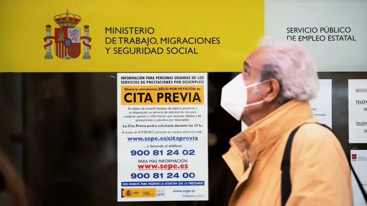 Un hombre con mascarilla mira un cartel del SEPE que explica c&oacute;mo solicitar el paro: 