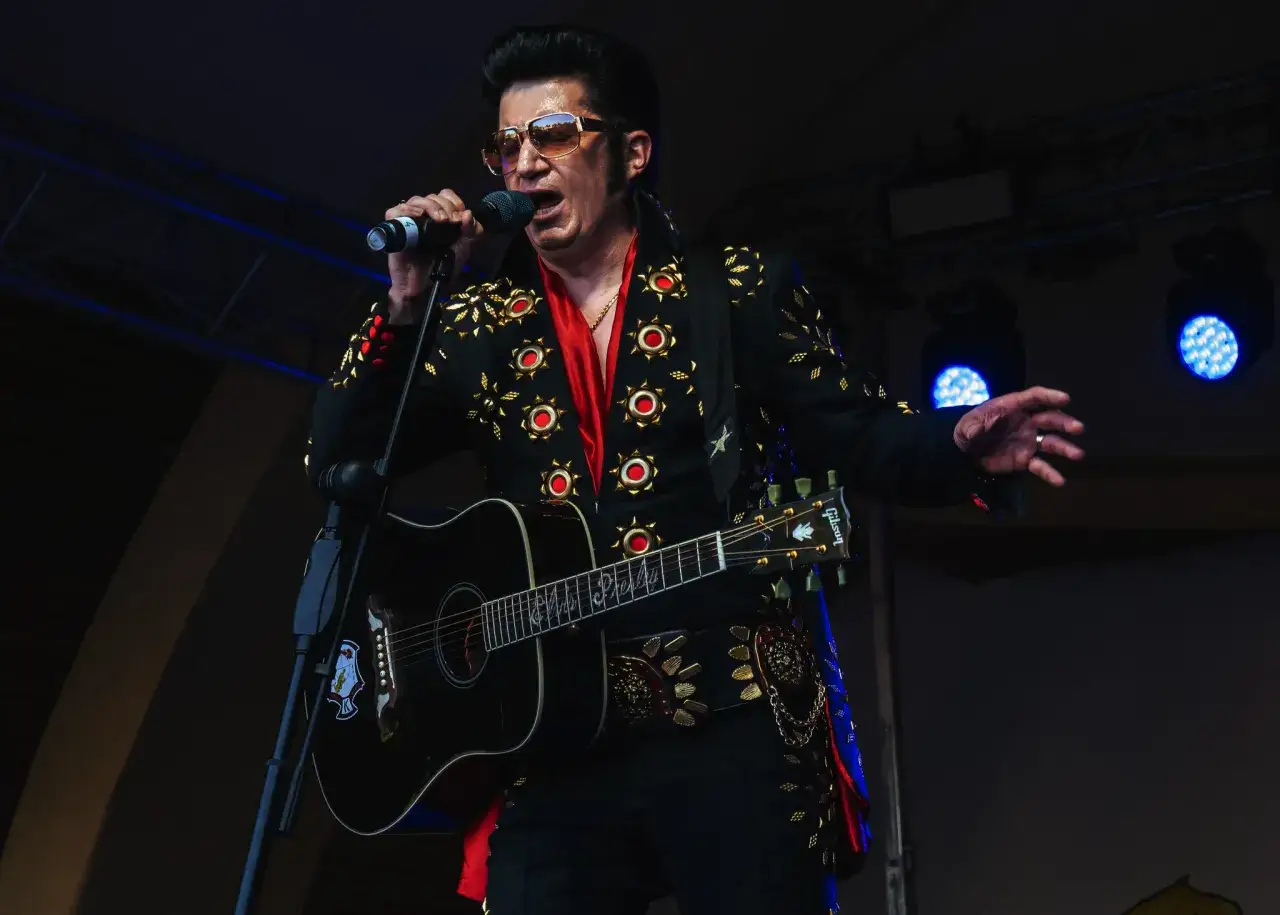 Polski Elvis Presley w błyszczącym stroju śpiewa do mikrofonu, grając na gitarze.