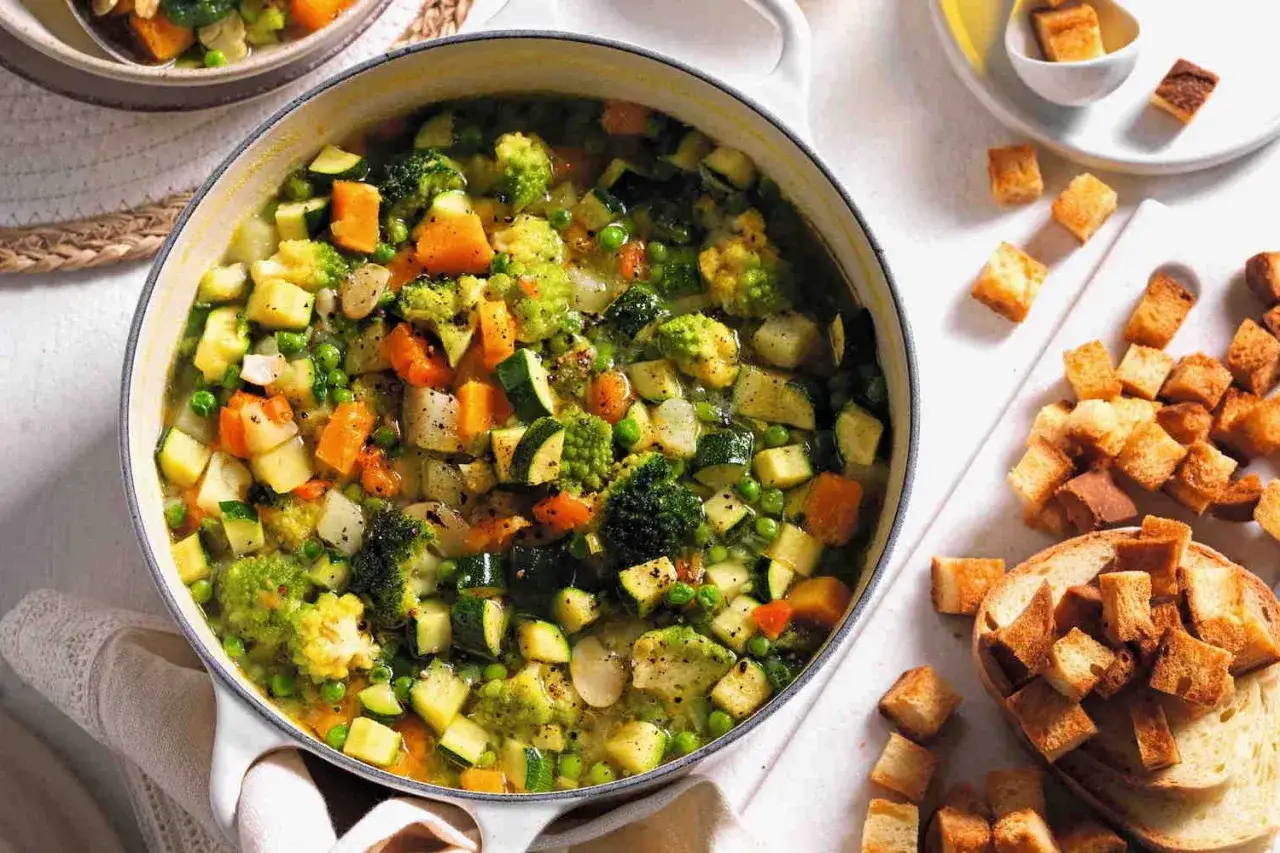 Un fumante minestrone di verdure, ricco di zucchine, carote, broccoli e piselli, pronto per essere gustato con crostini dorati.