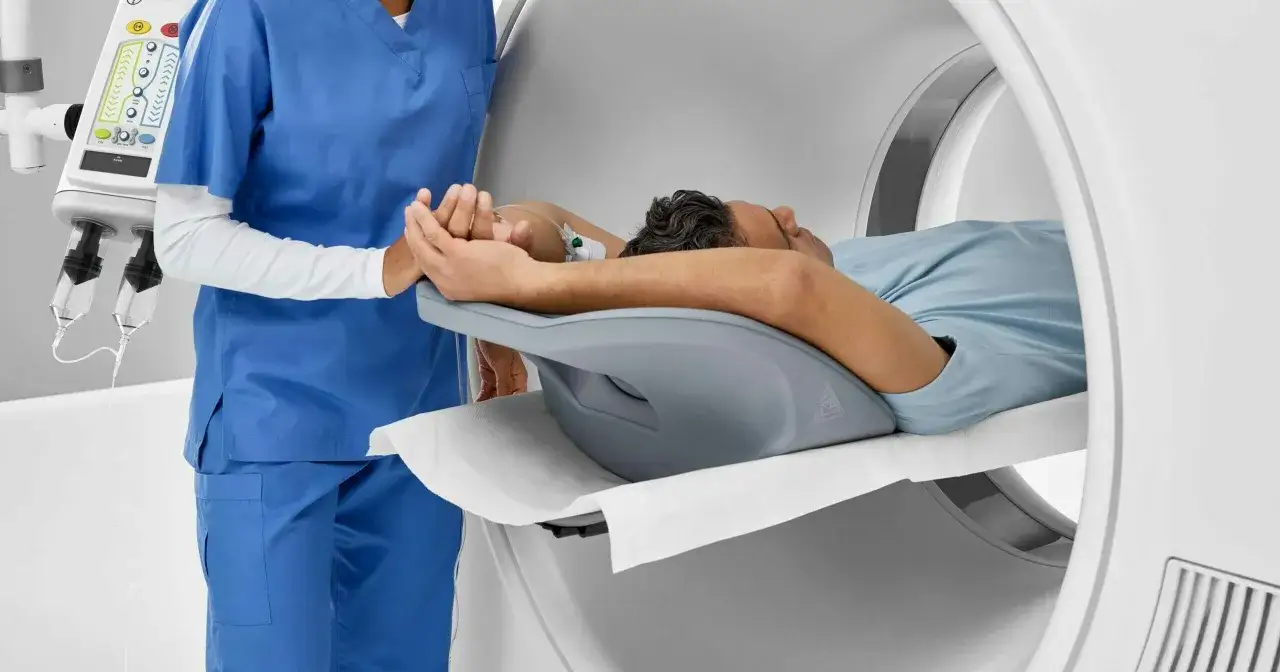 Pacjent leży na stole aparatu do angiografii, pielęgniarka trzyma go za rękę.