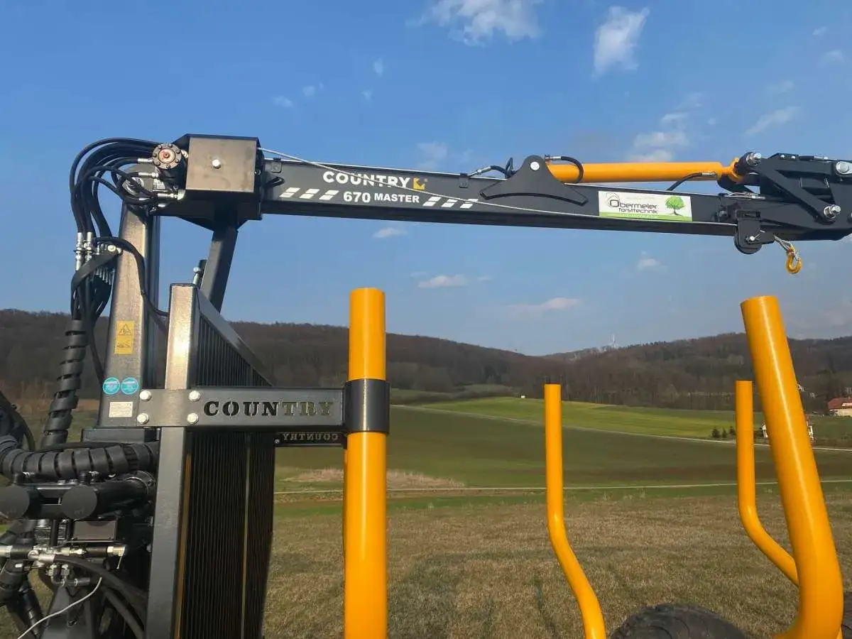 Ein COUNTRY 670 MASTER Forstkran Bausatz, bereit für den Einsatz im Wald. Gelbe Greifarme ragen aus dem robusten Stahlrahmen.