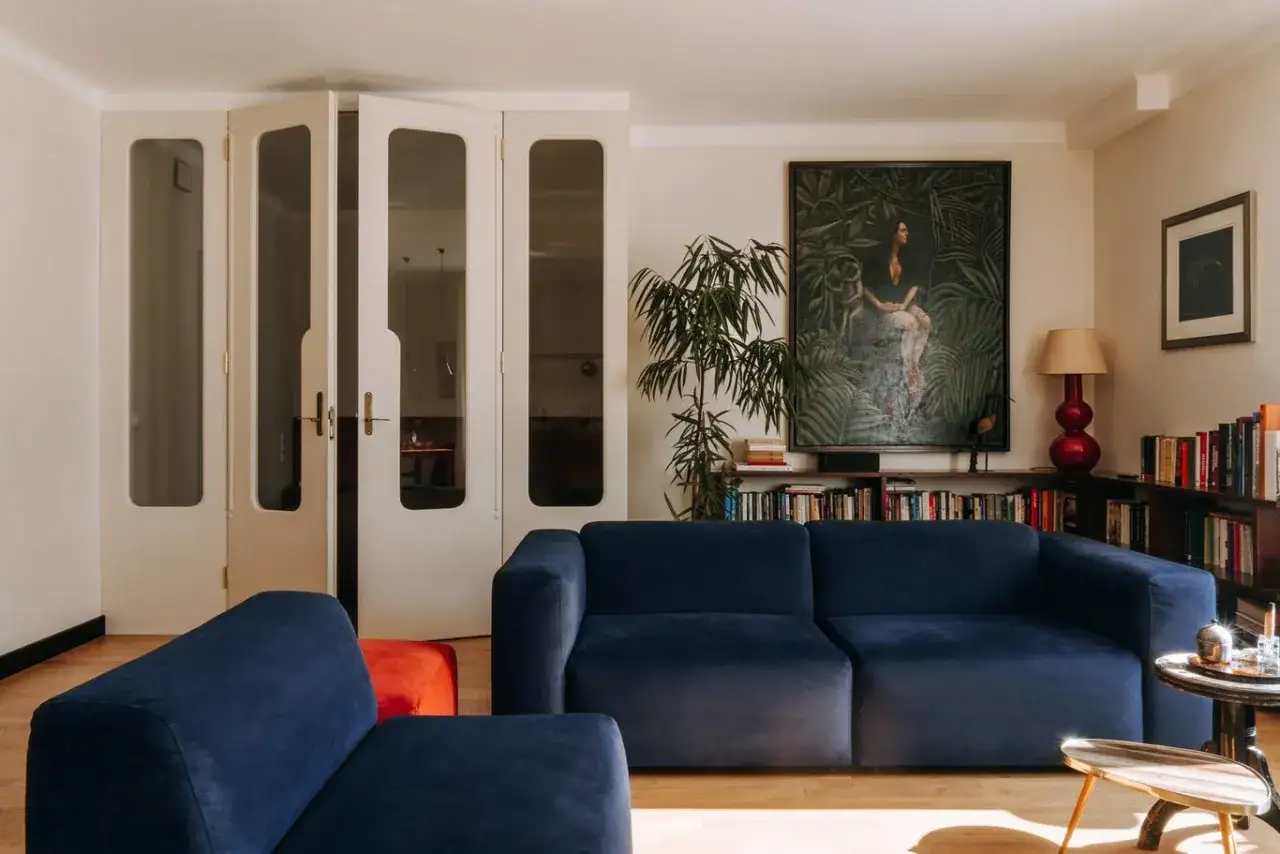 Przytulny salon z granatową kanapą, obrazem w dżungli i regałami pełnymi książek. Tak może wyglądać miejsce, gdzie mieszka sanah.