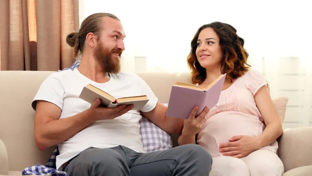 Pareja leyendo cuentos para adolescentes en el sof&aacute;. &Eacute;l le muestra un libro, ella sonr&iacute;e.