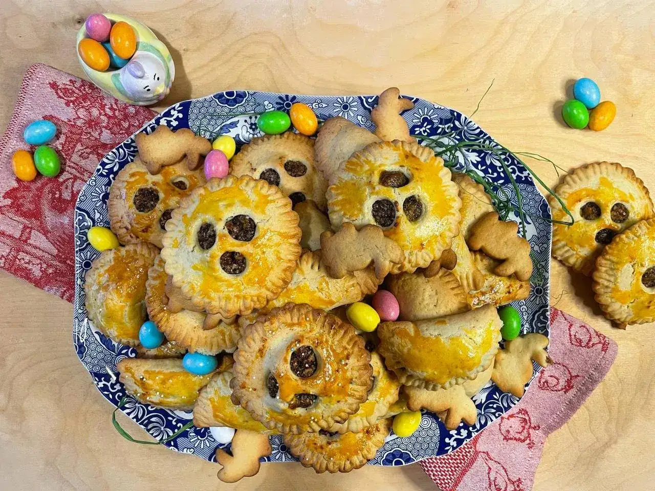 Piatto di nepitelle calabresi ricetta originale, dolcetti dorati con ripieno scuro, decorati con ovetti colorati e biscotti a forma di animali.